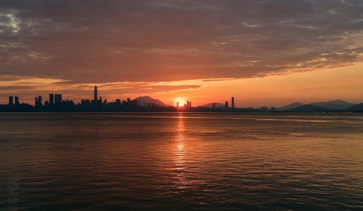 Silhouette einer Großstadt-Skyline am Wasser im orangefarbenen Abendlicht – Trump offen für Gipfel mit Putin und Xi in China